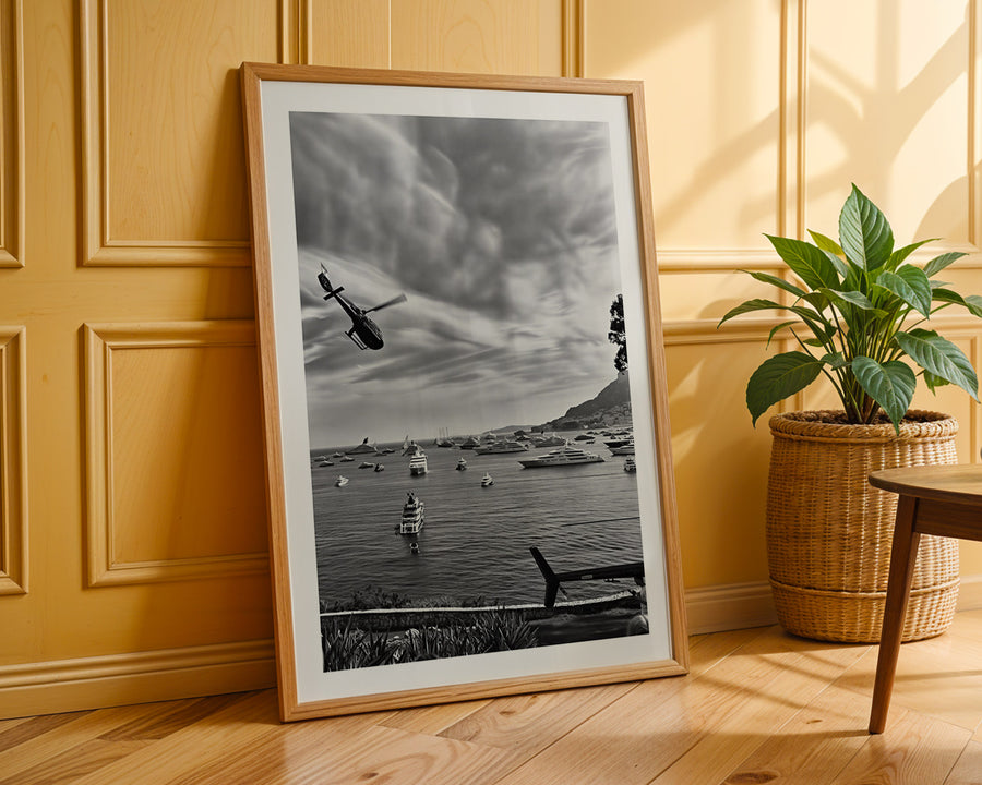 Framed black and white photograph of a coastal scene with boats and a helicopter, leaning against a wooden wall.