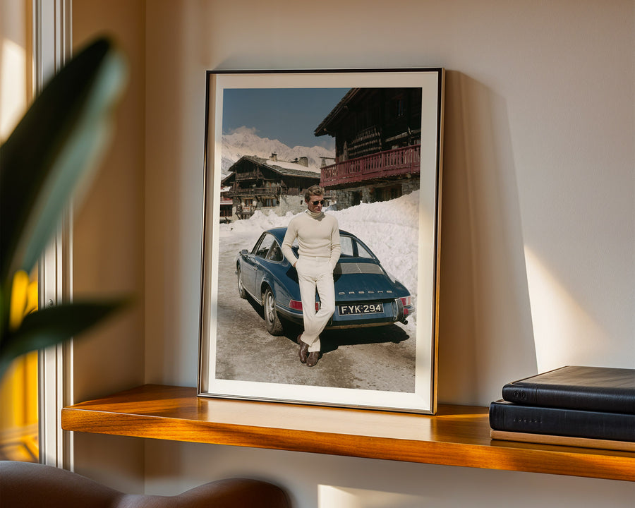 Framed photograph of a person standing next to a vintage car on a snowy mountain landscape, displayed on a shelf.