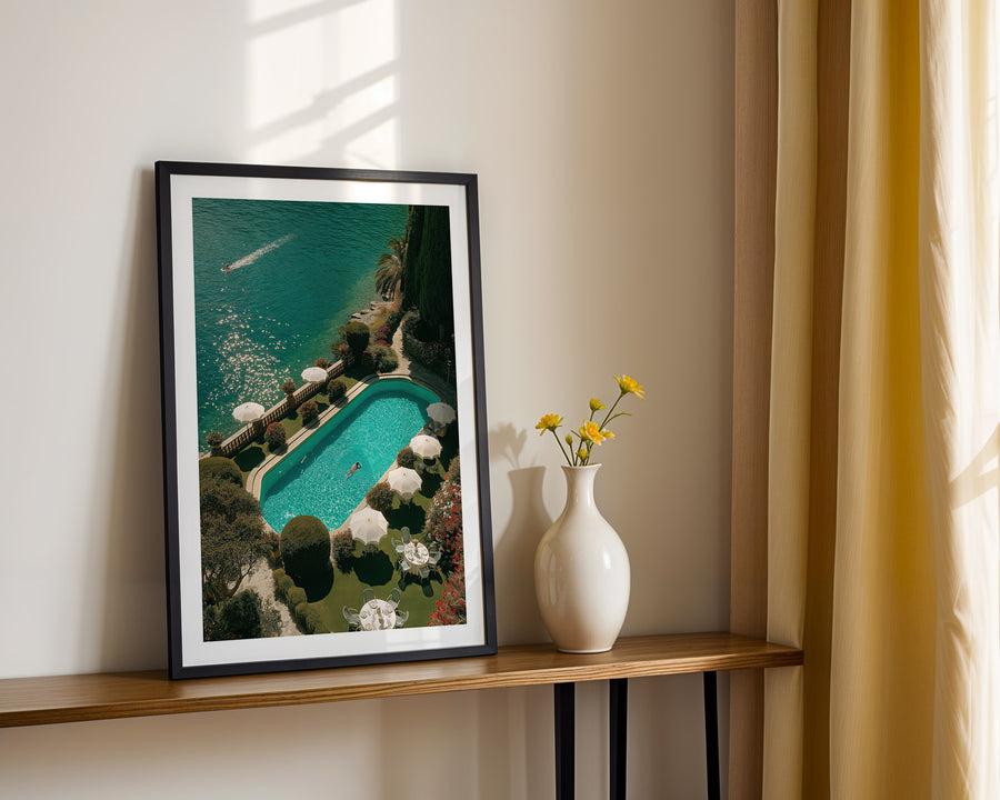 Framed artwork of a pool scene on a wooden shelf with a vase and flowers.