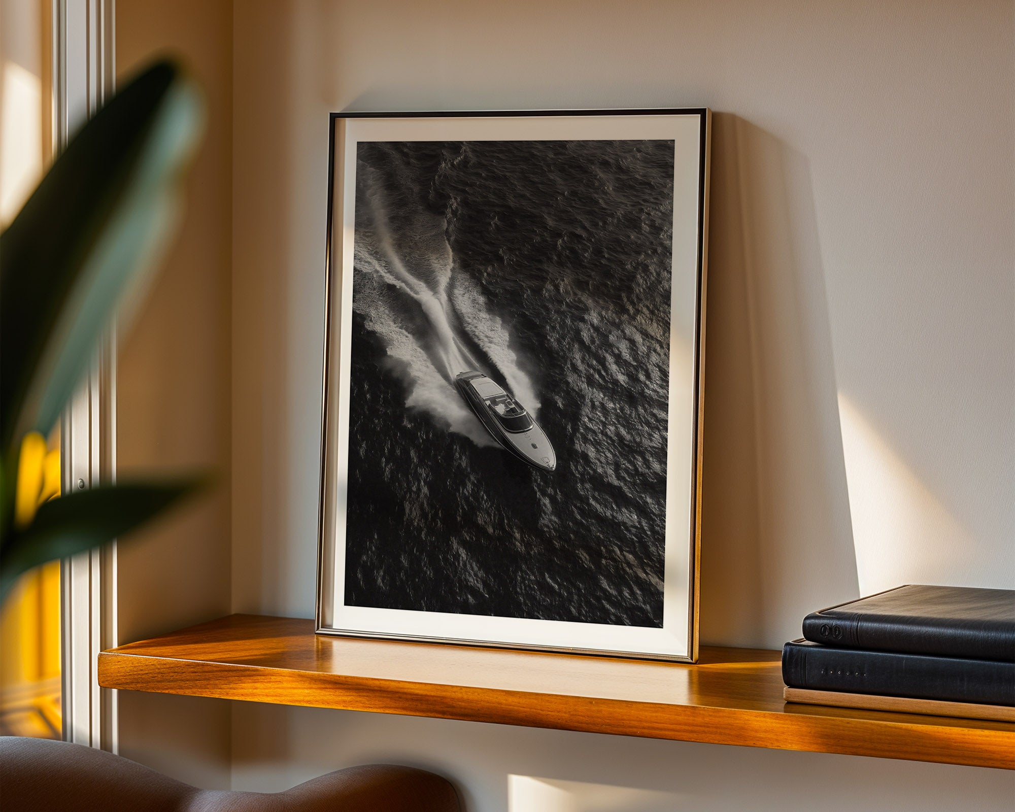 Framed black and white artwork on a wooden shelf with books and a plant.