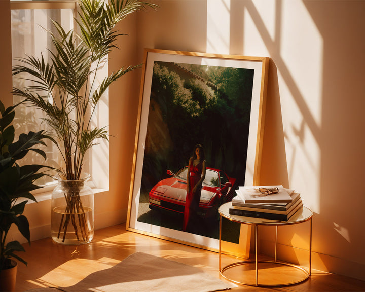 Framed artwork of a woman by a car on a wall next to a plant and small table.