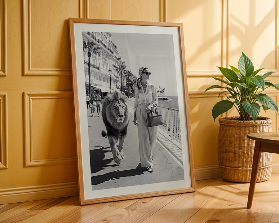 Framed black and white photo of a woman walking a lion on a city street, placed against a wooden wall with a plant beside it.