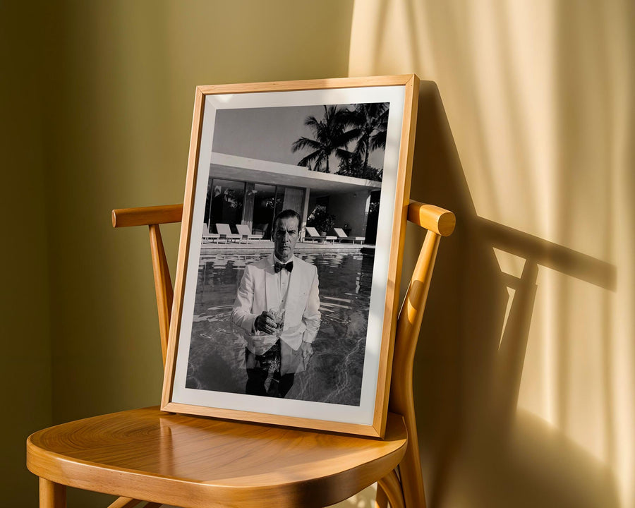 Framed black and white photo of a man by a pool on a wooden chair with a warm light.