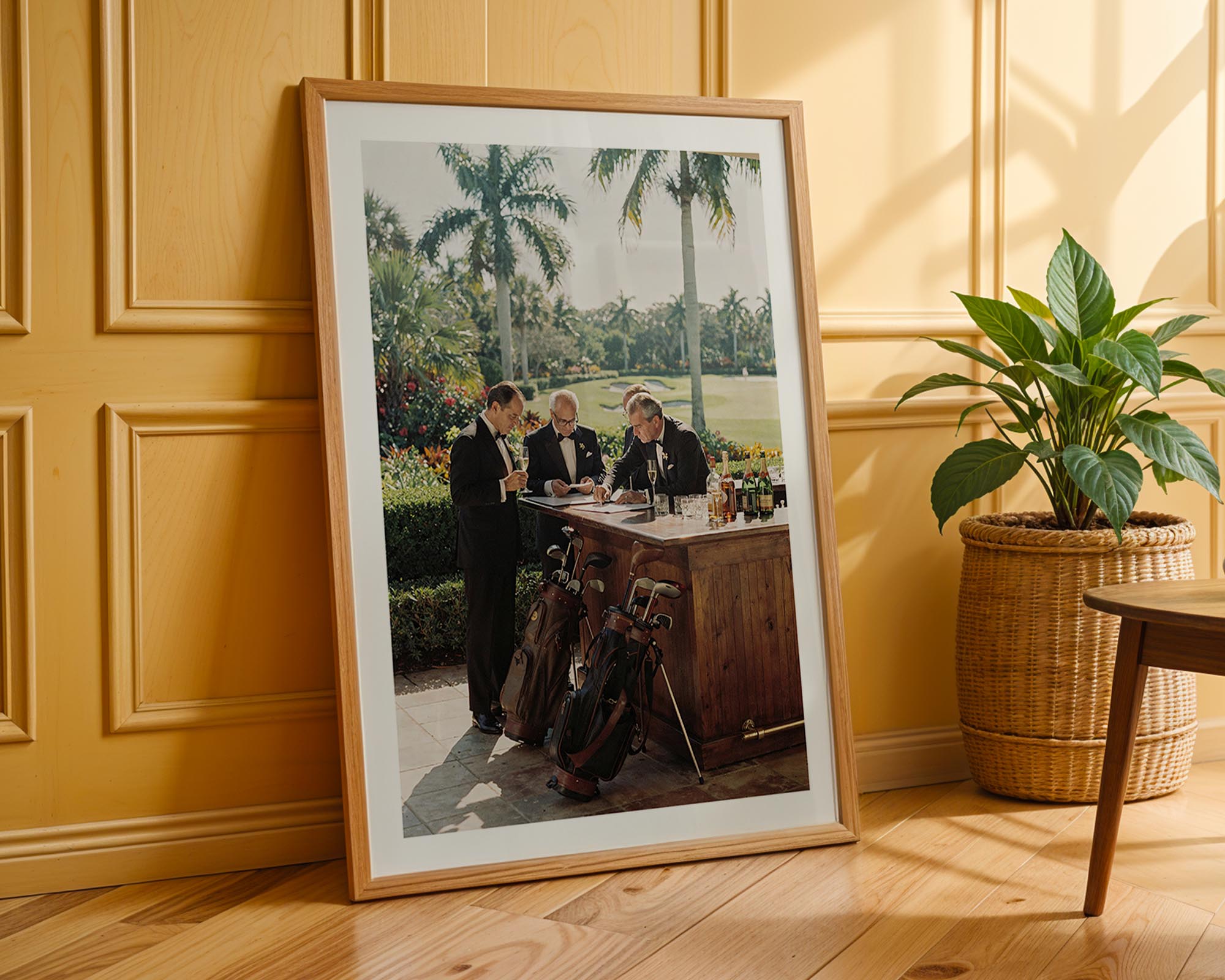 Framed photograph of a group of people at a table outdoors, leaning against a wooden wall with a plant in the foreground.