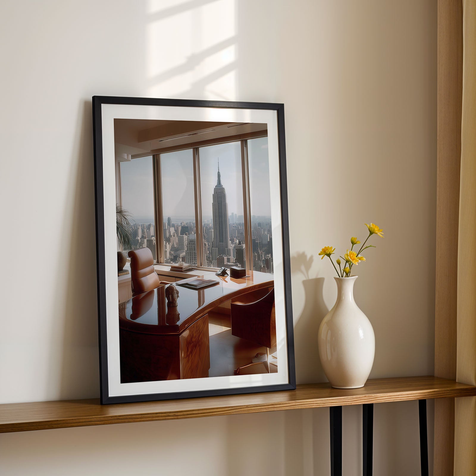 Framed artwork of a cityscape on a wall above a wooden shelf with a vase and flowers.