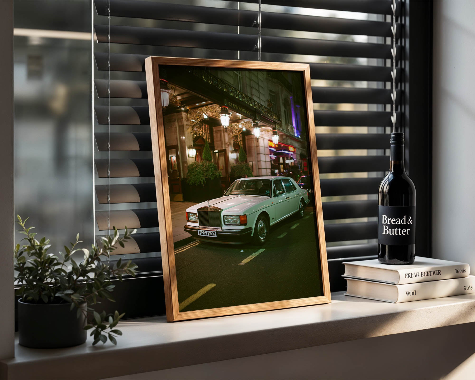 Framed photograph of a vintage car on a shelf with a bottle of 'Bread & Butter' and books.