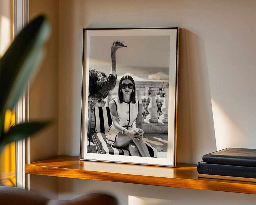 Framed black and white photograph of a woman on a shelf with books and a plant.