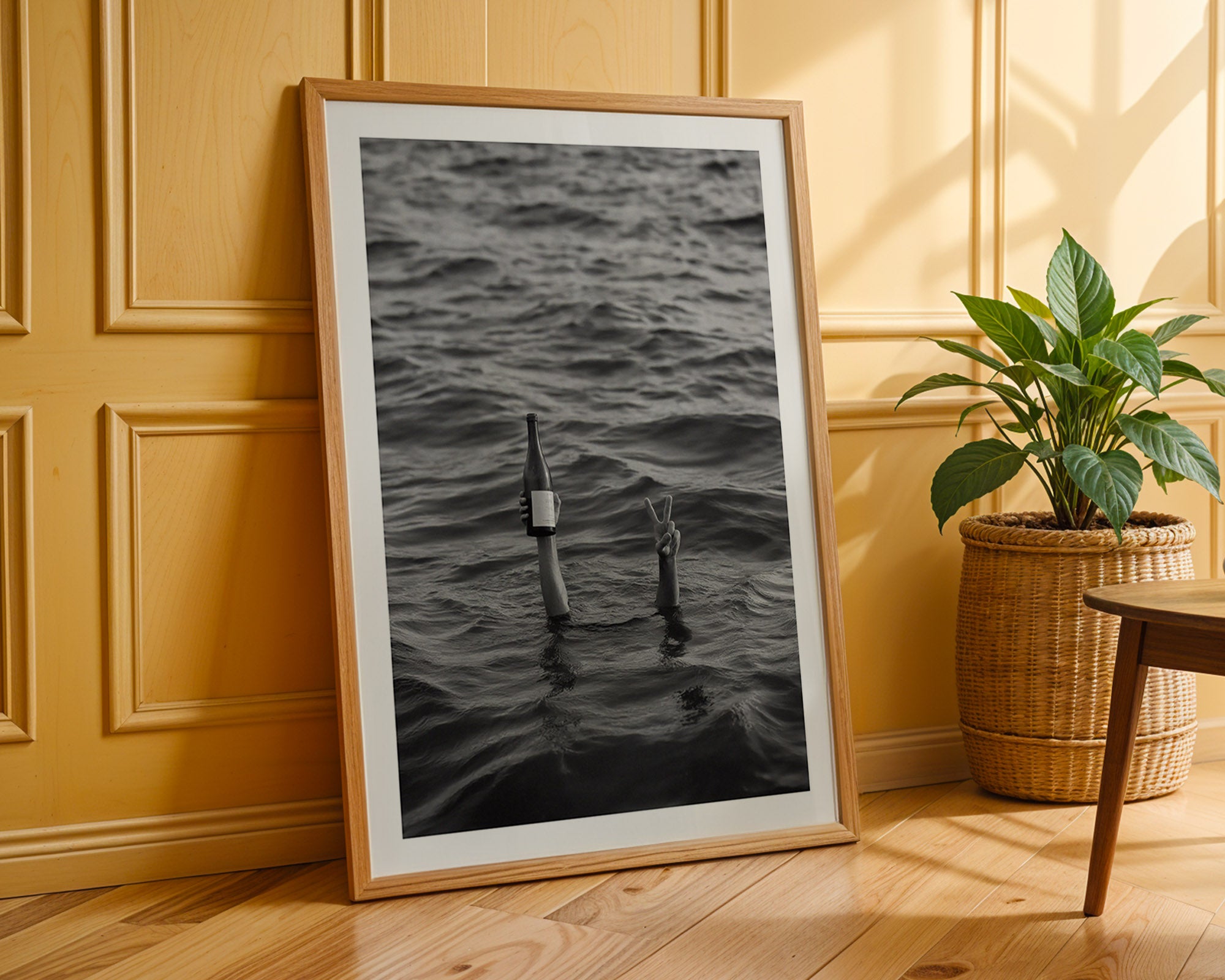 Framed black and white photograph of a fishing rod in water on a wooden floor with a plant in the background.