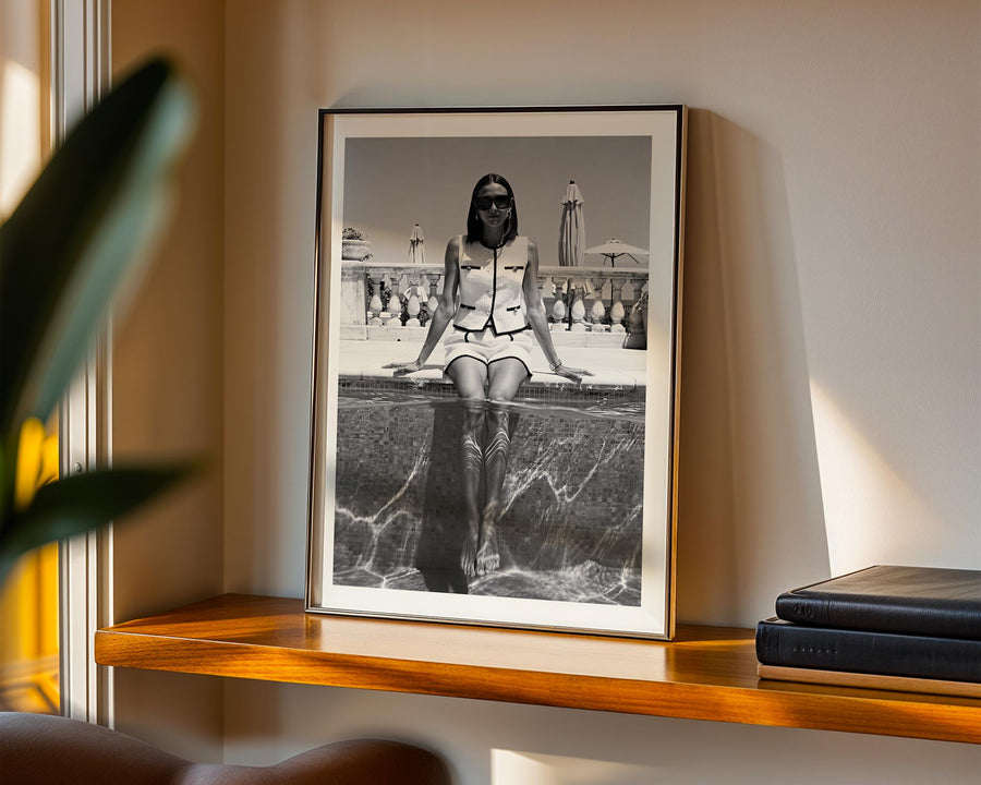 Framed black and white photograph of a woman sitting by a pool on a wooden shelf.