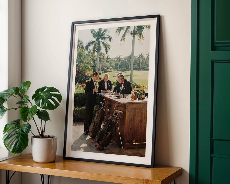 Framed photograph of a golf course scene on a wooden table with a plant beside it.