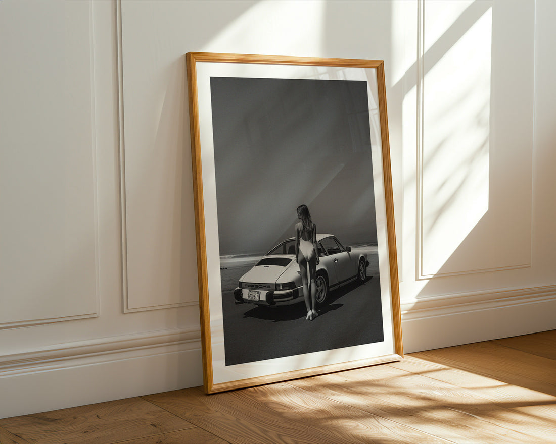 Framed black and white photograph of a person next to a car on a wall.