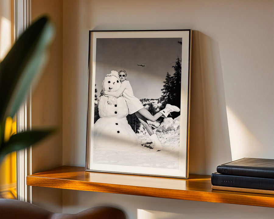 Framed black and white photograph of a person with a snowman on a shelf.