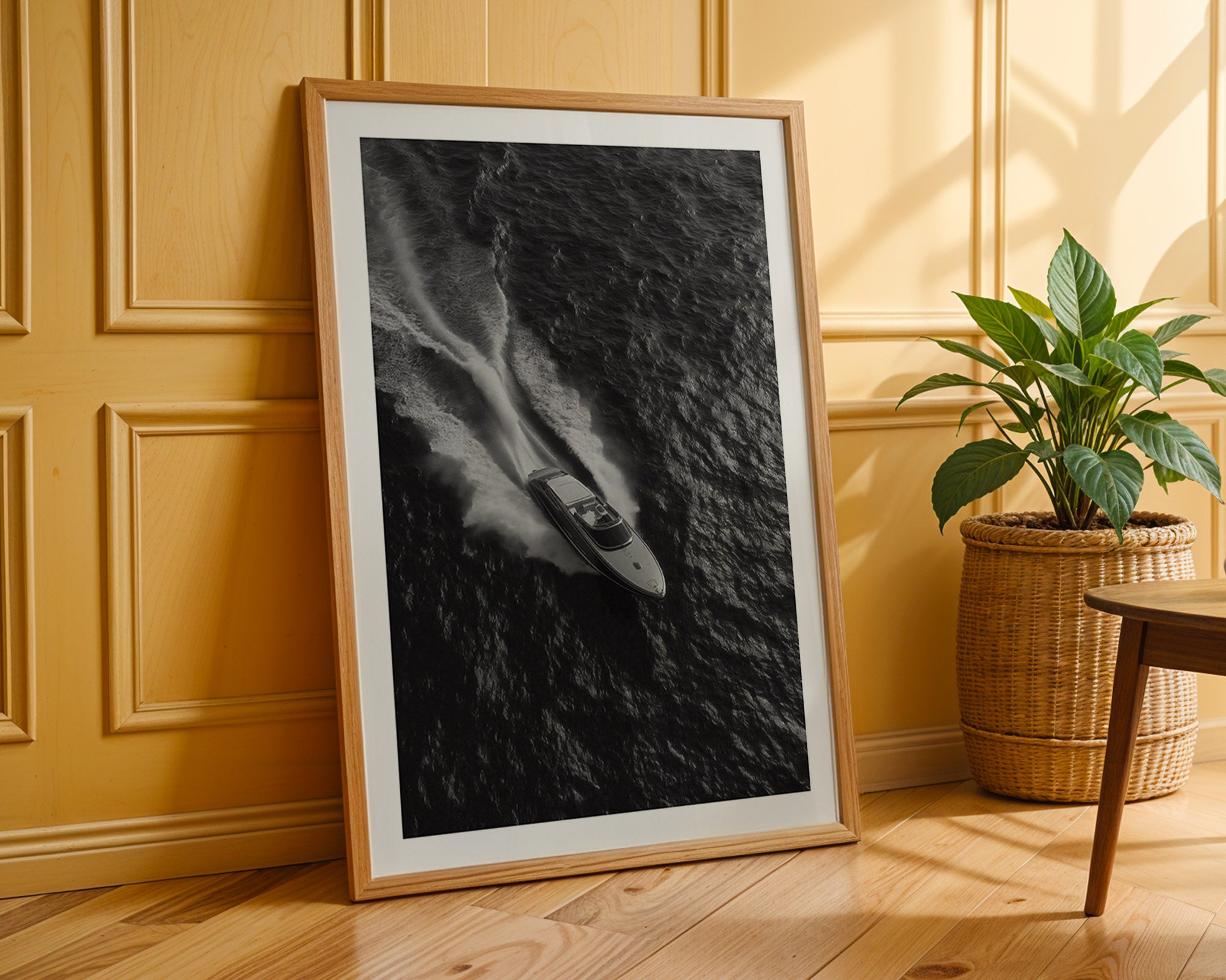 Framed black and white artwork leaning against a wooden wall with a plant in the background.