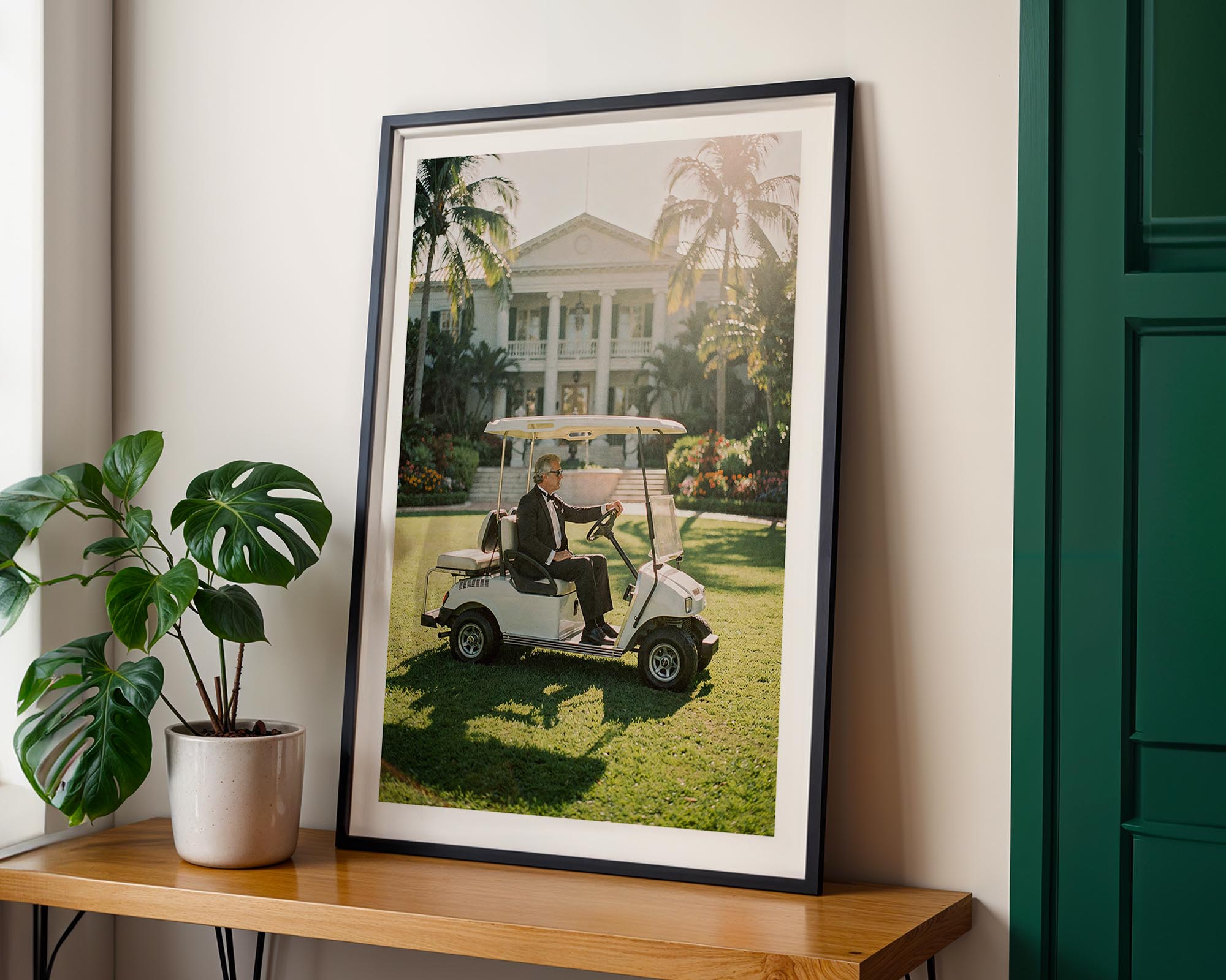 Framed photograph of a person on a golf cart in a garden setting, placed on a wooden shelf with a plant.
