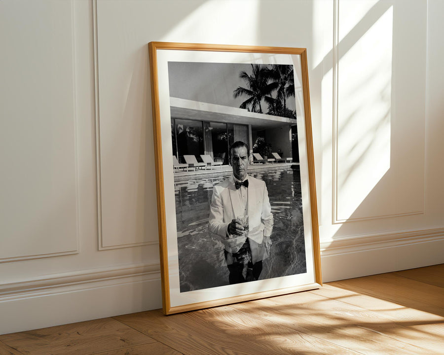 Framed black and white photograph of a man by a pool on a wall with sunlight casting shadows.