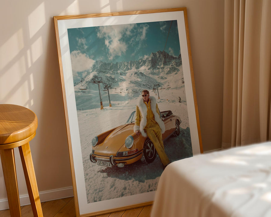 Framed photograph of a person in a yellow outfit sitting on a vintage car with mountains in the background, leaning against a beige wall.