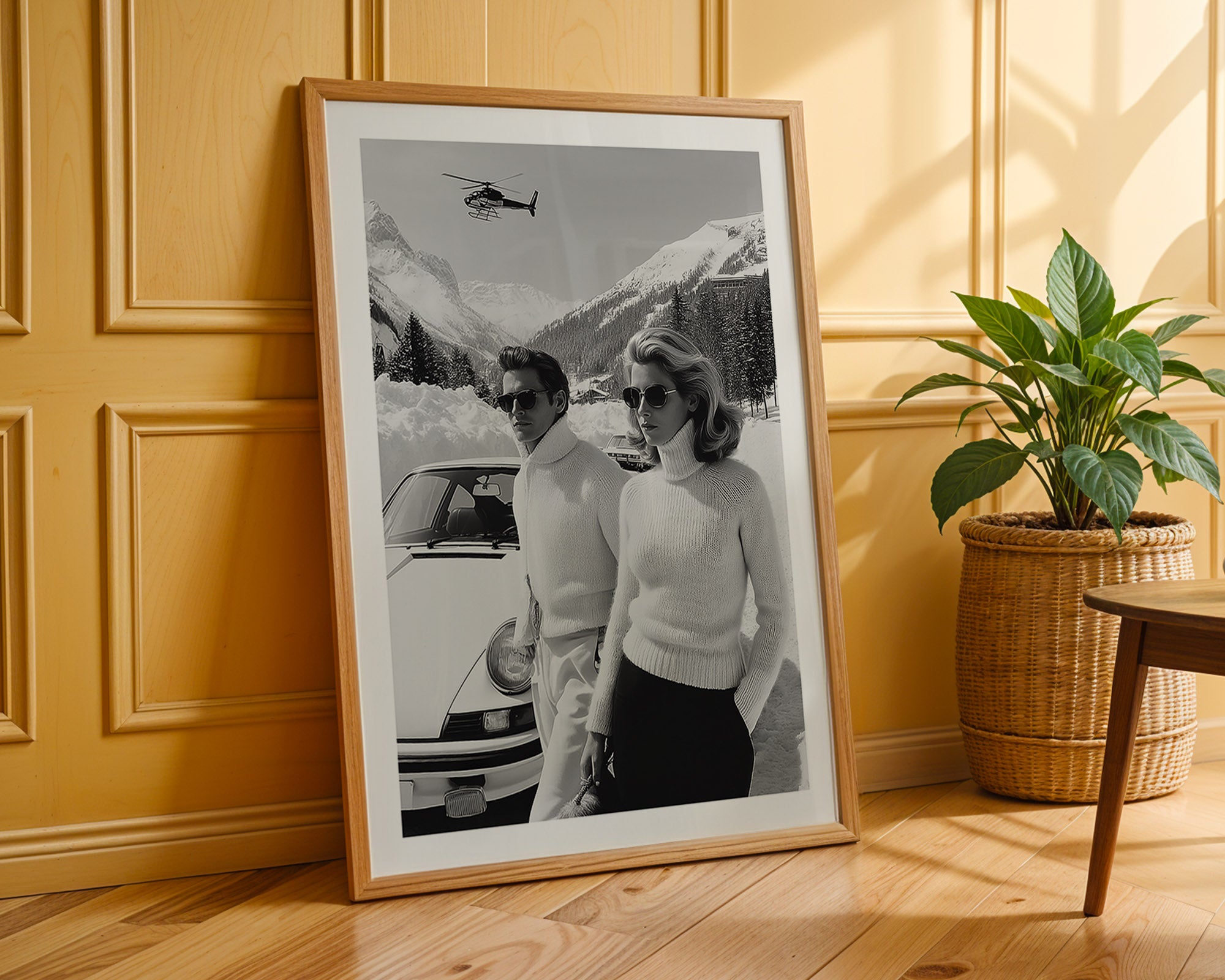 Framed black and white photo of a couple by a car with mountains in the background, placed on a wooden floor.