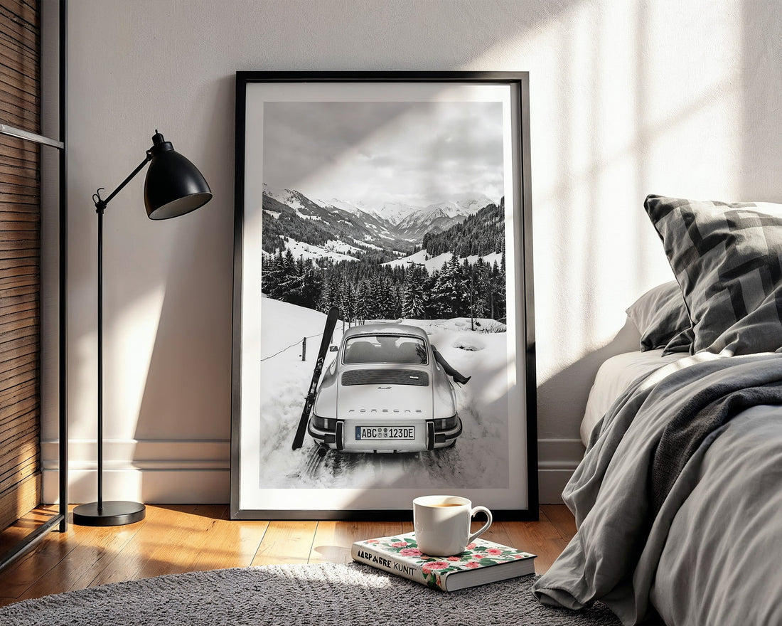 Framed black and white print of a snowy mountain scene with a 911 Porsche car, placed in a bedroom.