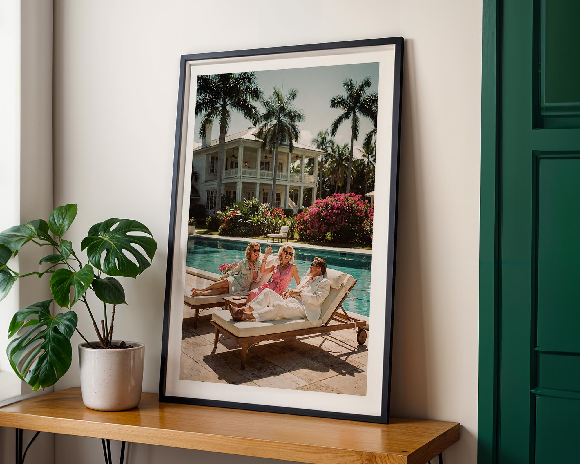 Framed photograph of people by a pool with palm trees, on a wooden shelf with a plant.