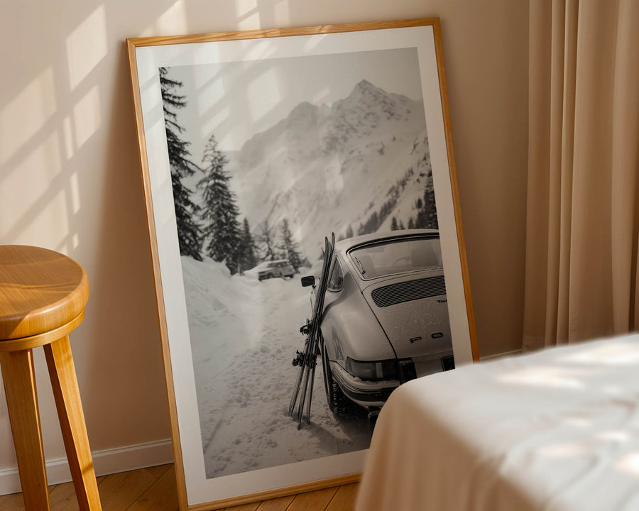 Framed photograph of a snowy mountain scene with a Porsche 911 and skis, leaning against a wall.