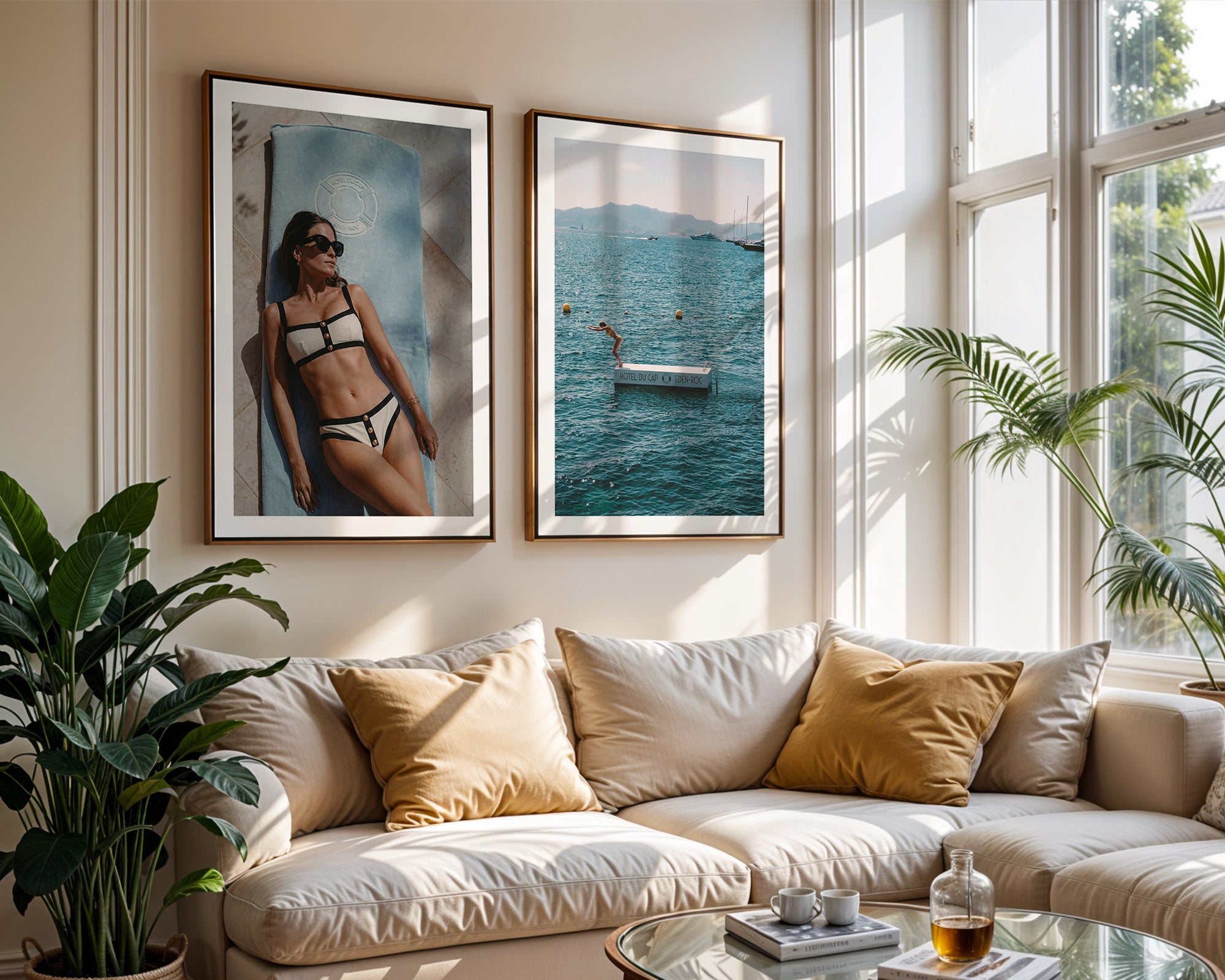 Living room with a beige sofa, decorative pillows, and framed posters of a woman in a bikini and a person diving in the water at Hotel du Cap-Eden-Roc.