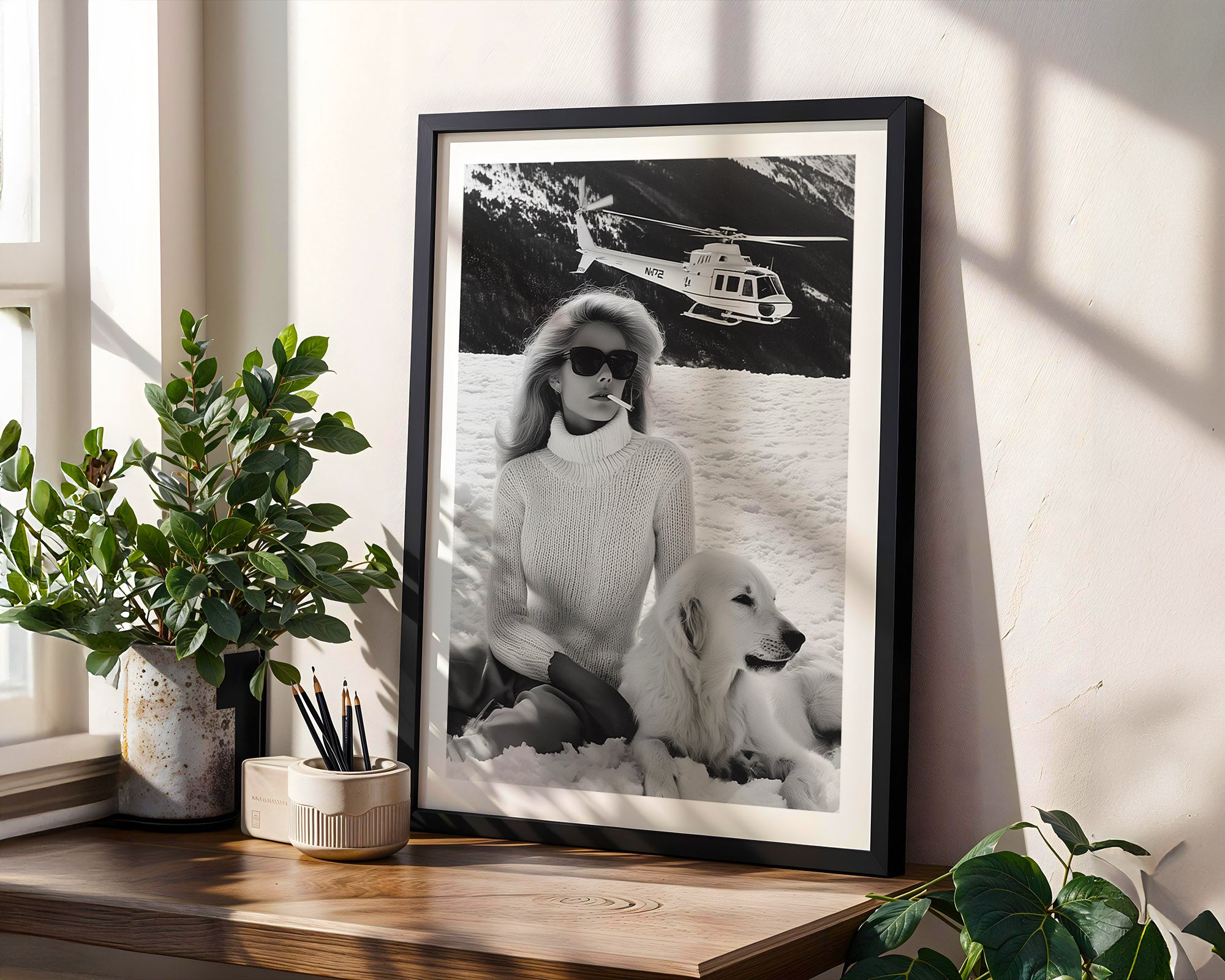 Framed black and white photo of a woman with a dog on a wooden shelf with plants.