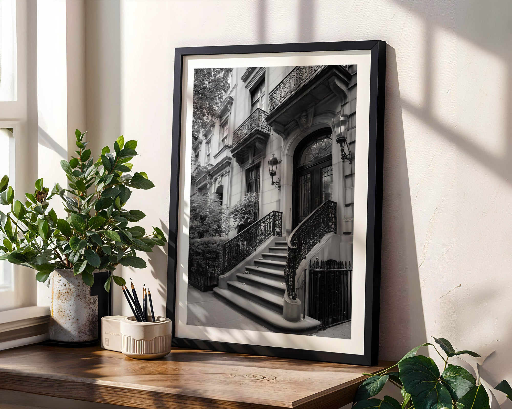 Framed black and white print of a staircase on upper eastside with plants and a window.