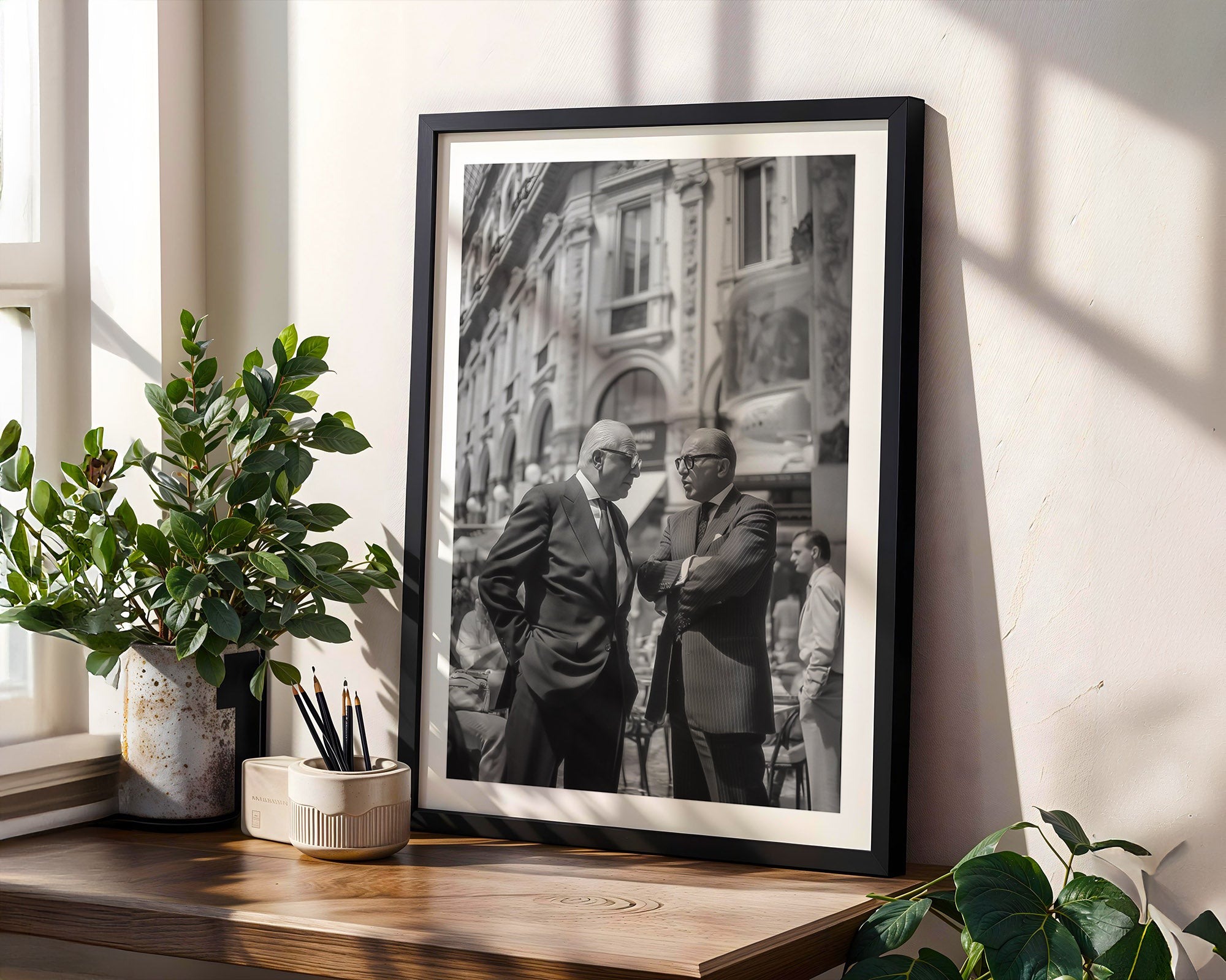 Framed black and white photograph of two men on a wooden shelf with plants.