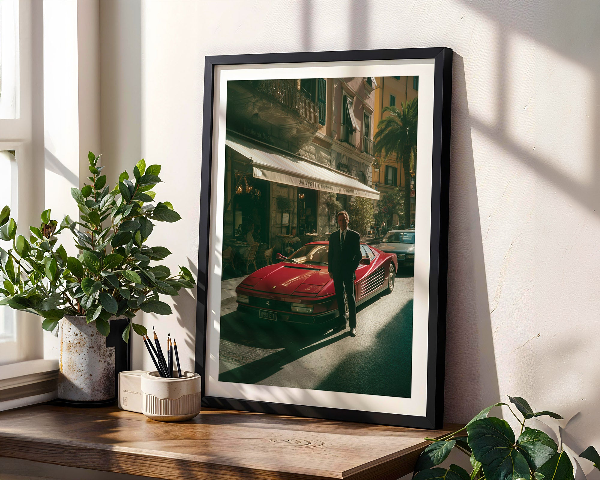 Framed photograph of a man standing next to a red Ferrari on a city street, placed on a wooden surface with plants.