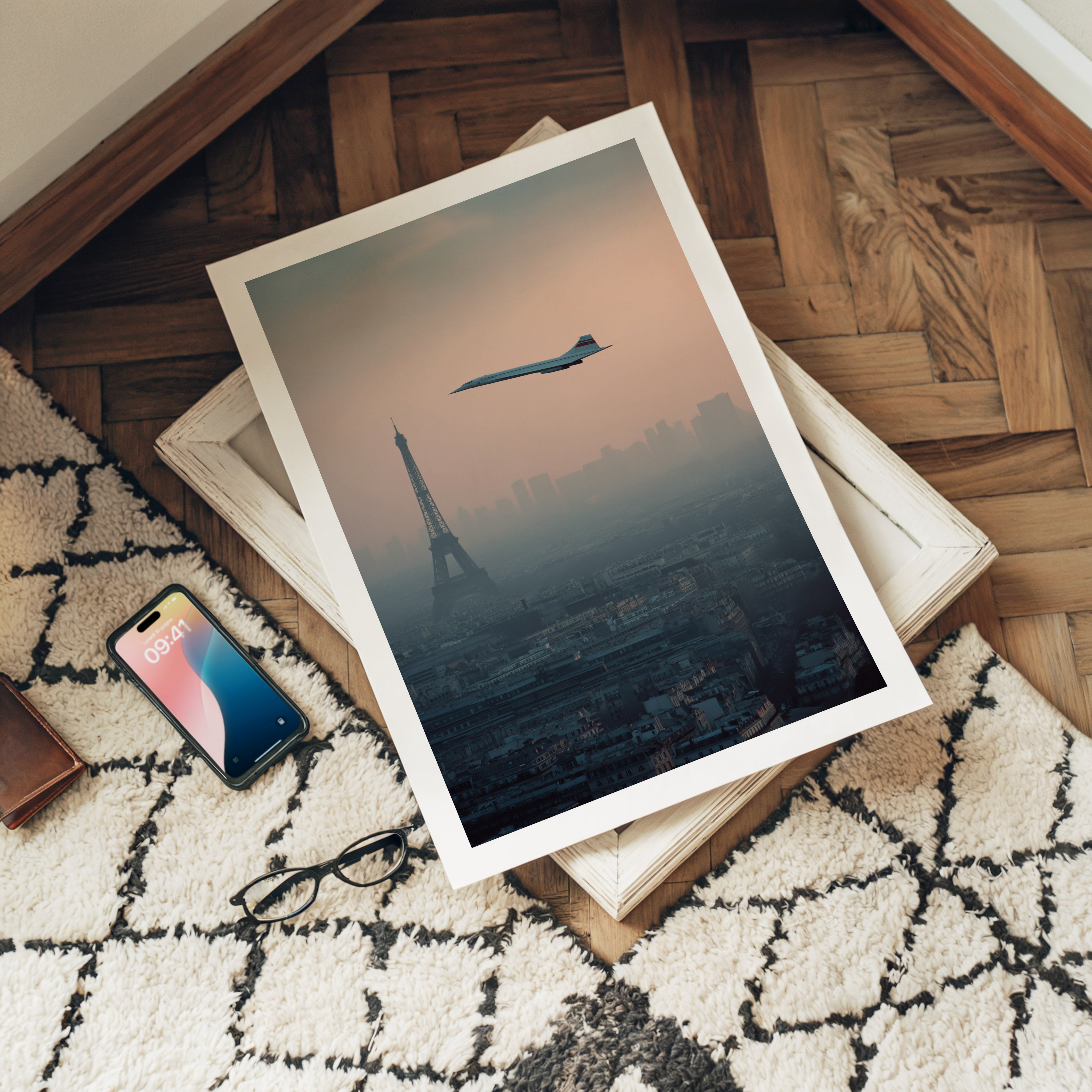 Framed artwork of a cityscape with a plane flying over, placed on a surface with a phone and glasses.