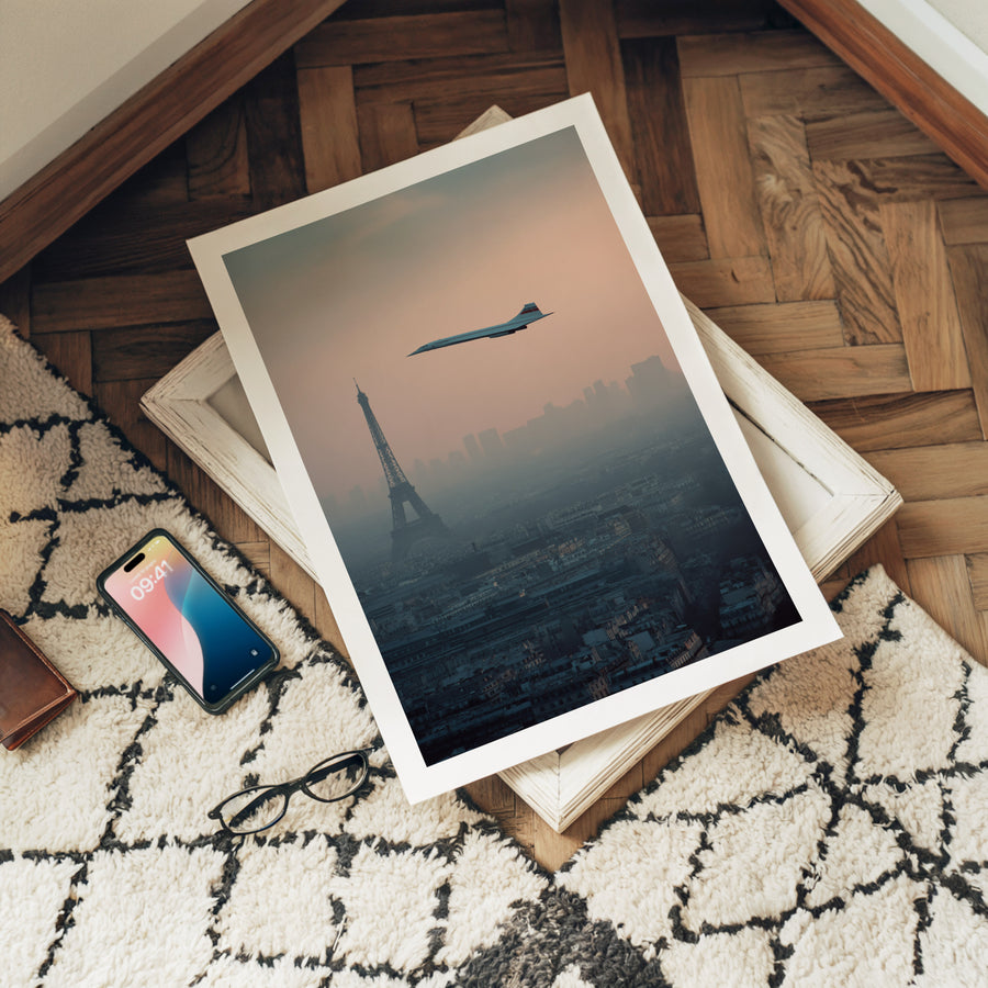Framed artwork of a cityscape with a plane flying over, placed on a surface with a phone and glasses.