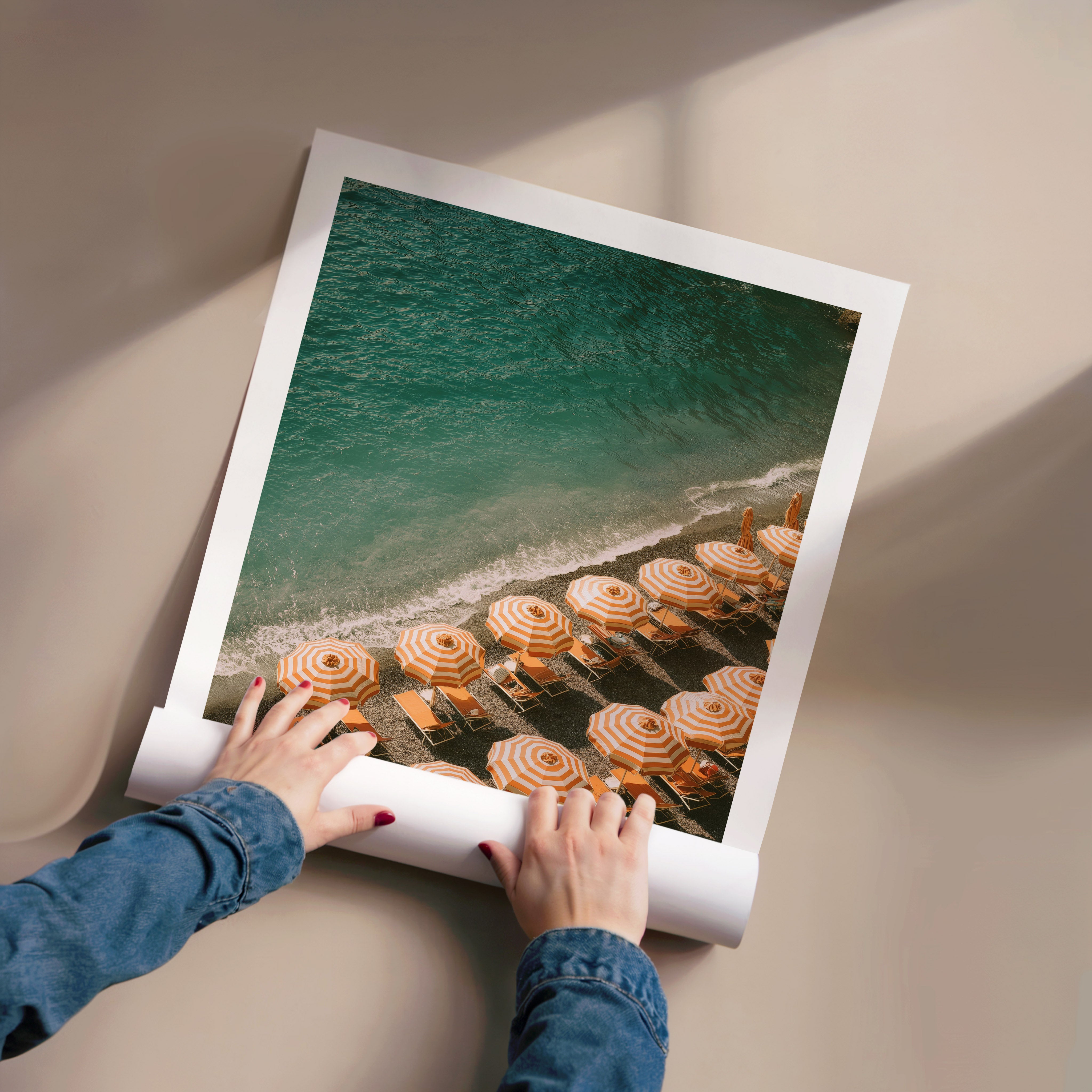 Person unrolling a large photo of a beach scene with umbrellas and chairs.