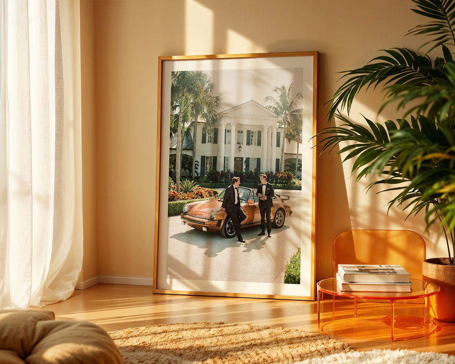 Framed photograph of two people by a vintage car in a living room with a plant and table.