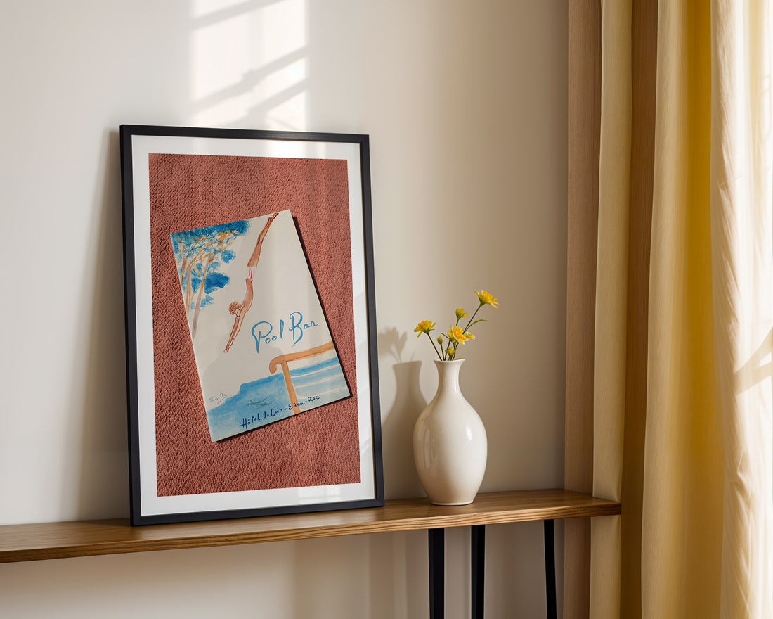 Framed artwork on a shelf with a vase of flowers. Hôtel du Cap-Eden-Roc