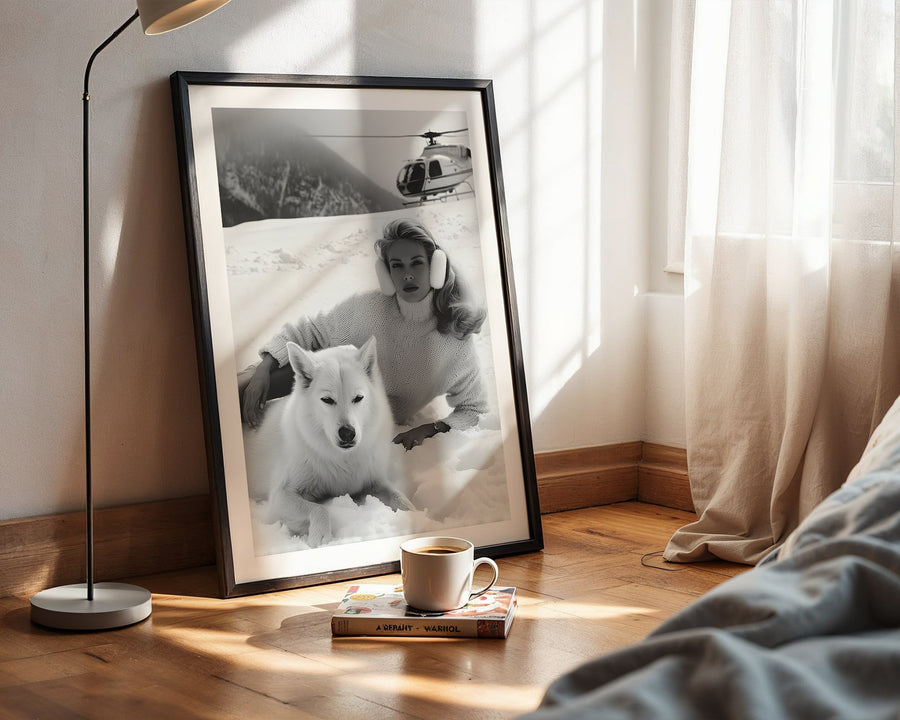 Framed black and white photo of a person with a dog on a wooden floor next to a lamp and books.