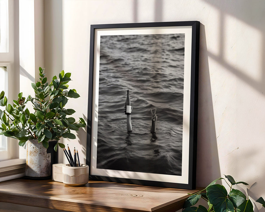 Framed black and white artwork of bottles in water on a wooden shelf with plants.