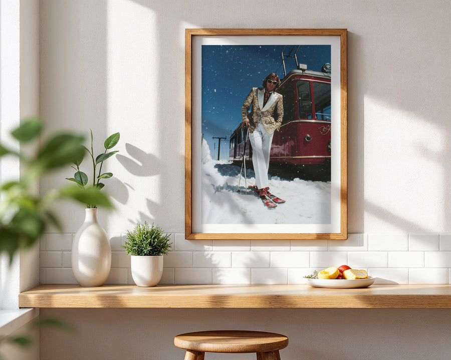 Framed artwork of a person skiing next to a red tram on a wall above a wooden shelf with plants and fruit.