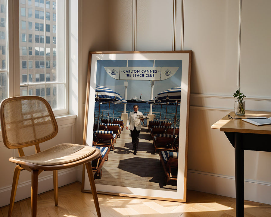 Framed photograph of a man in a suit on a dock, leaning against a wall with a chair and table in the foreground.