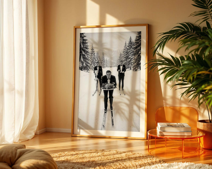 Framed black and white photograph of people skiing in a snowy landscape on a wall in a sunlit room.