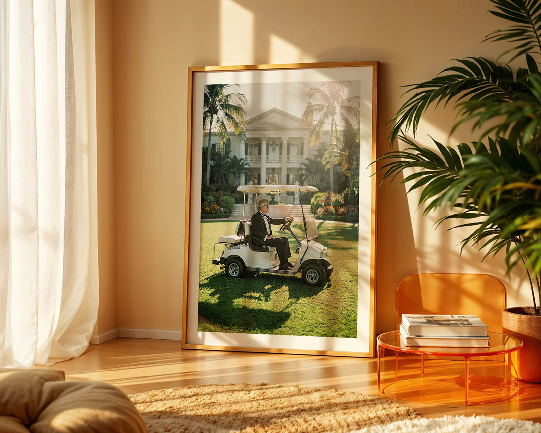 Framed photograph of a man on a golf cart in a garden, displayed in a room with a plant and table.