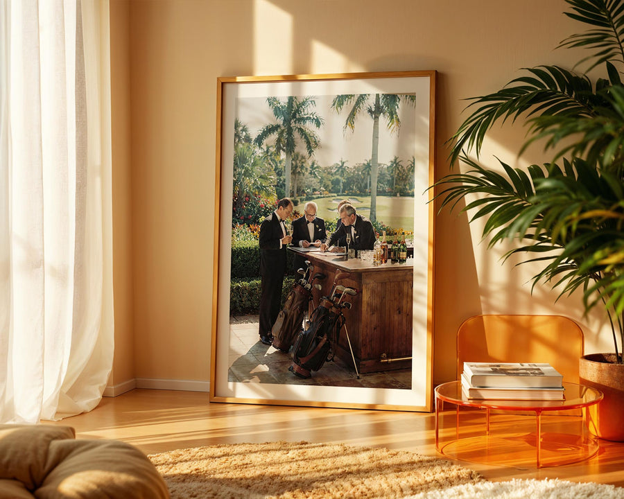 Framed artwork of a golf scene in a living room with a plant and table.