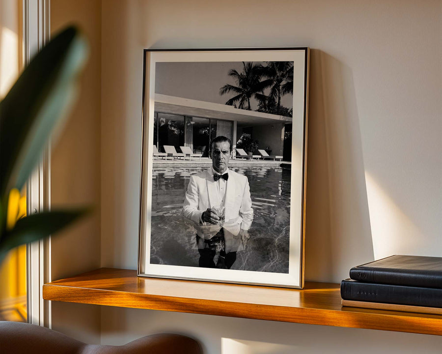 Framed black and white portrait of a man by a pool on a wooden shelf.