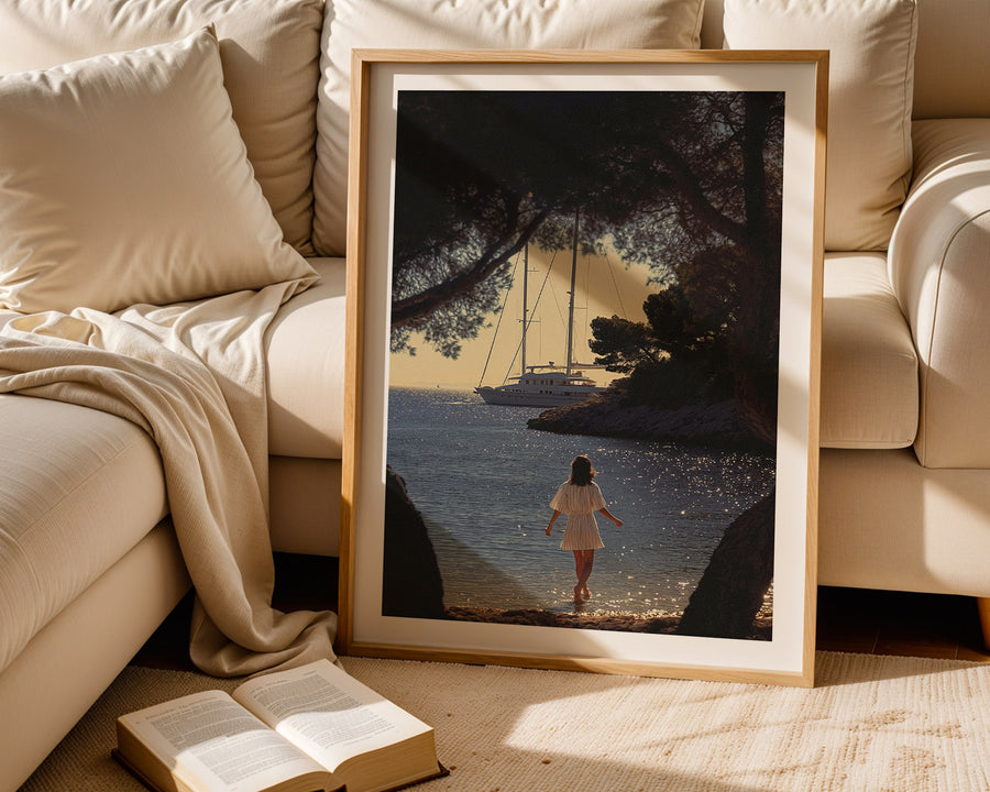 Framed artwork of a woman walking by a lake with a sailboat, placed on a beige sofa.