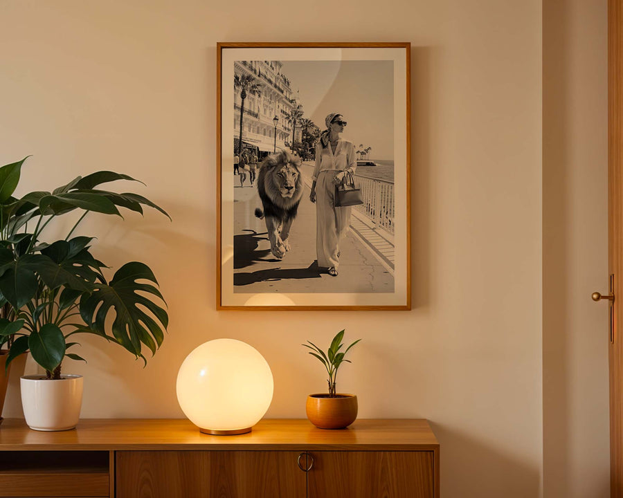 Framed black and white photo of a person with a lion on a wall above a wooden cabinet with decorative plants and a lamp.