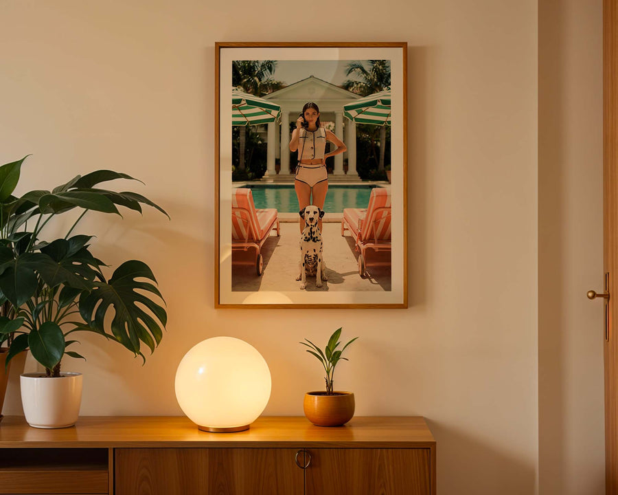 Framed artwork of a woman by a pool on a wall above a wooden cabinet with decorative items.