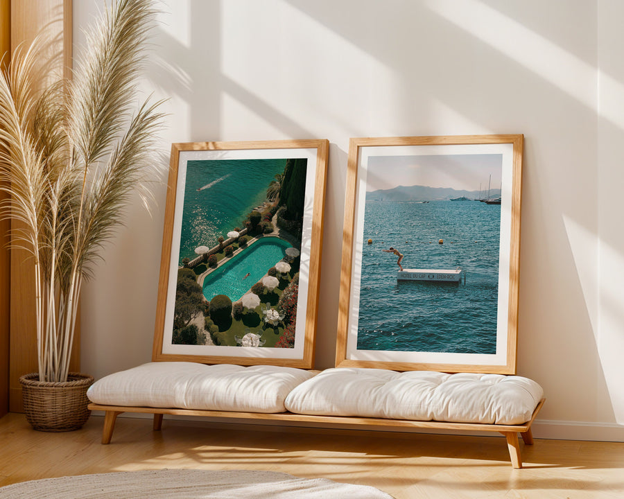 Two framed pictures of landscapes on a wooden bench with a plant in the background.