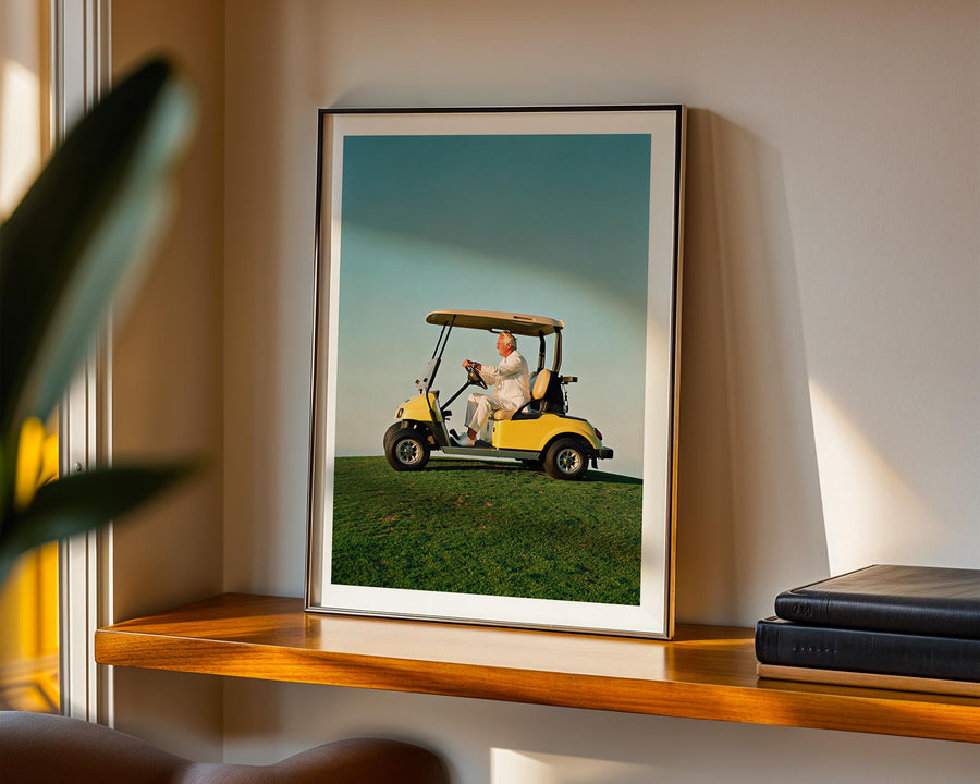 Framed picture of a man in a golf cart on a grassy field, displayed on a shelf.