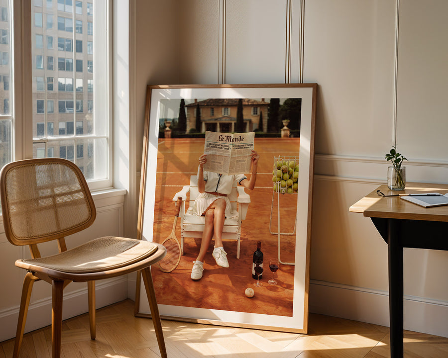 Framed artwork of a person reading a newspaper in a room with a window and chair.