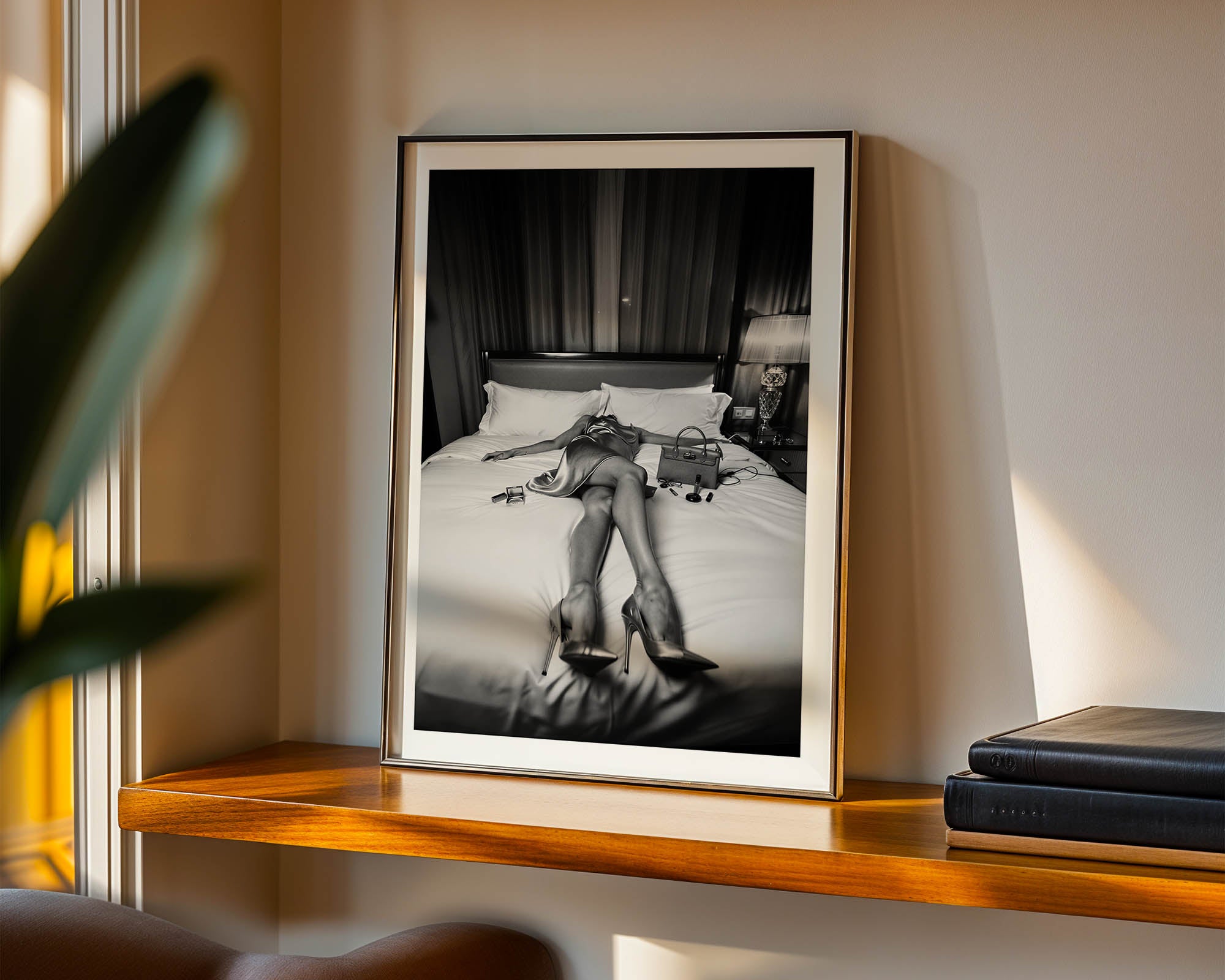 Framed black and white photograph of a person on a bed in a room with a lamp and books.