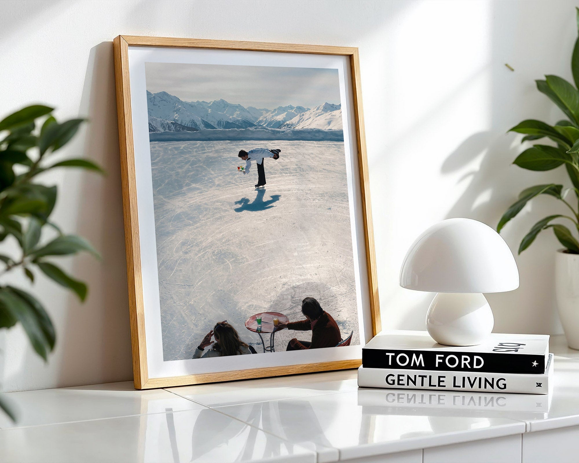 Framed photograph of a person in the Swiss alps and mountains, placed on a shelf with a white lamp and books.